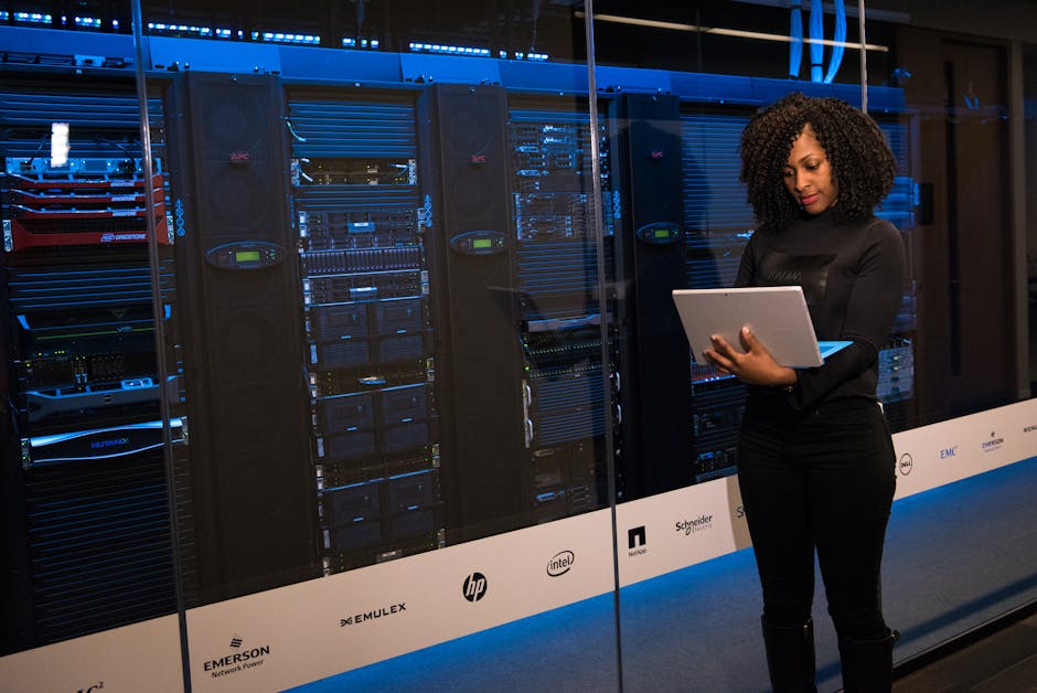 A female engineer using a laptop while monitoring data servers in a modern server room