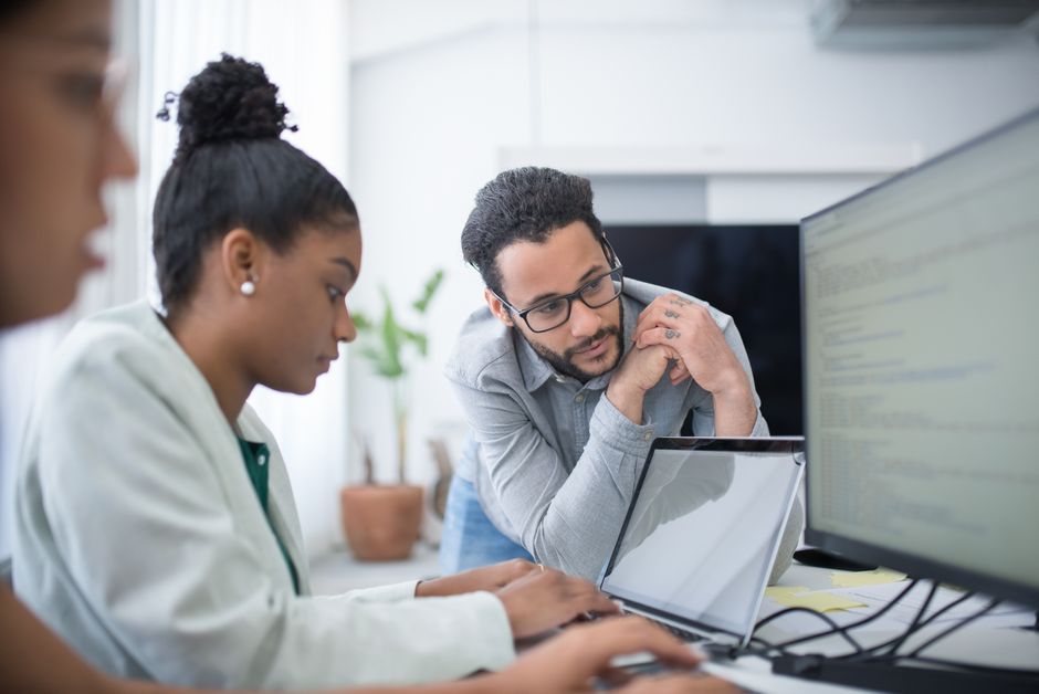 Two people collaborate in a modern office setting, focused on computer work.